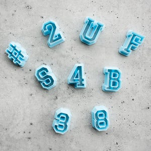 May include: A collection of light blue plastic cookie cutters in the shapes of the numbers 2, 3, 4, 8, the letters U, F, B, S, and a hashtag symbol. Each cutter features a thick, raised border and a hollow center for cutting dough shapes.