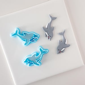 Könnte beinhalten: Drei Delfin-Ausstecher, zwei sind blau und einer ist grau. Die blauen Ausstecher sind offen und der graue Ausstecher ist geschlossen.