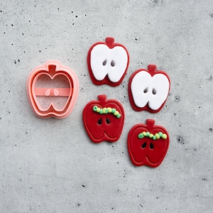 May include: A set of four red apple-shaped cookie cutters, two with white centers and two with green and white sprinkles, and a pink apple-shaped cookie cutter.