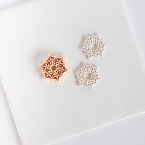 May include: A set of three snowflake-shaped cookie cutters. One is a light brown color, and the other two are off-white. The cutters have a detailed, openwork design, perfect for holiday baking or craft projects.