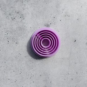 以下が含まれることがあります： 5つの紫色のプラスチック製の丸いクッキーカッターのセットで、互いに重ねられています