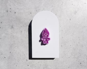May include: A bright purple troll figurine with a tall, textured hairstyle and a wide smile. The figure is centered on a smooth, white, arch-shaped display board, creating a clear contrast between the vibrant purple color and the white background.