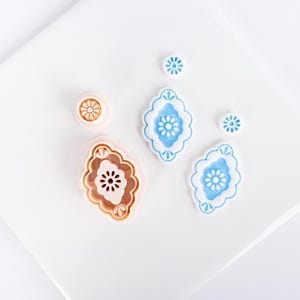 Puede incluir: Un conjunto de cortadores de galletas decorativos en varias formas y tamaños. Los cortadores incluyen una forma redonda, dos formas de almendra y dos pequeñas formas de flor. Los cortadores son en tonos marrón claro y azul, con un fondo blanco.