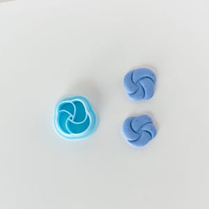 May include: Two blue fondant decorations shaped like a three-dimensional swirl, and a blue plastic cookie cutter in the shape of a swirl.