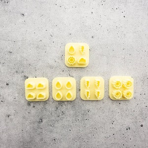 Puede incluir: Cinco cortadores de galletas de plástico amarillo con diferentes diseños de temática meteorológica. Los cortadores están dispuestos en forma de pirámide sobre un fondo gris.