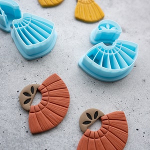 Puede incluir: Dos pares de pendientes de arcilla de color terracota con forma de abanico y un peque&ntilde;o dise&ntilde;o de hoja. Los pendientes est&aacute;n al lado de dos juegos de moldes de pl&aacute;stico azul para hacer los pendientes.