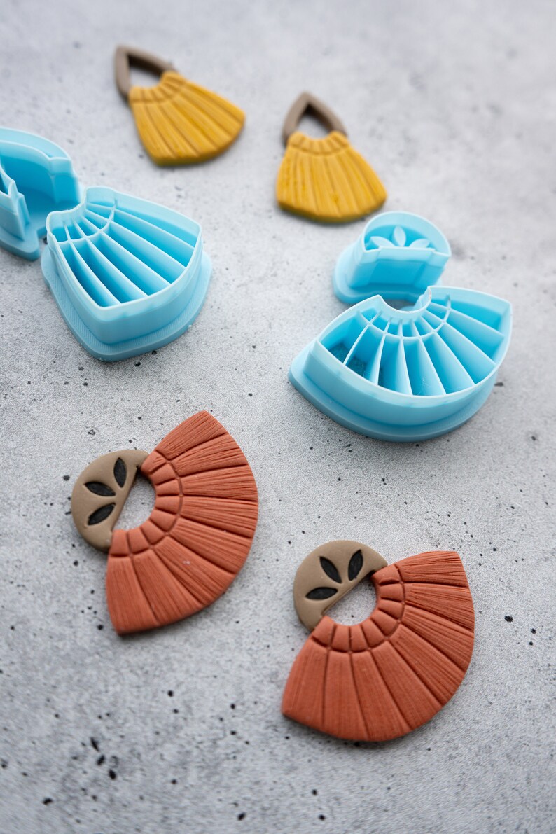 Puede incluir: Dos pares de pendientes de arcilla de color terracota con forma de abanico y un peque&ntilde;o dise&ntilde;o de hoja. Los pendientes est&aacute;n al lado de dos juegos de moldes de pl&aacute;stico azul para hacer los pendientes.