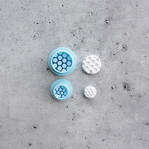 May include: Three round cookie cutters, two are light blue with a honeycomb pattern and one is white with a honeycomb pattern.