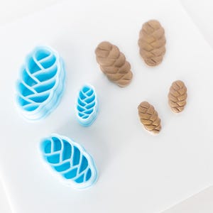 May include: A set of blue and brown plastic cookie cutters shaped like pine cones. The cutters are arranged on a white surface.