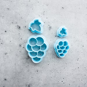 May include: A set of four blue plastic cookie cutters shaped like grapes and leaves.
