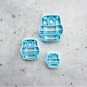 May include: Three light blue plastic cookie cutters in varying sizes, each featuring a central circular detail and a rounded rectangular frame with horizontal bars, designed for shaping dough into a specific character or object form.