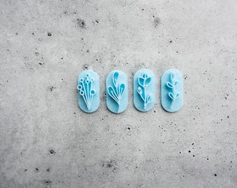 May include: Four light blue oval-shaped clay cutters, each featuring a distinct raised botanical design. The designs include a cluster of berries, a multi-leaf stem, a single tulip-like flower, and a small leafy branch, all arranged in a horizontal row.