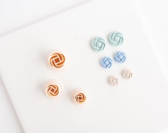 May include: A collection of circular cutters and finished buttons featuring a geometric square-in-circle pattern. The set includes three light peach plastic cutters and six buttons in varying sizes and colors, including sage green, blue, and beige.