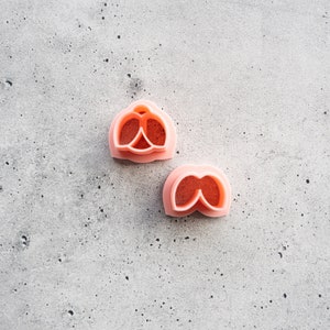 May include: Two pink plastic flower cookie cutters on a gray textured surface. The cutters are shaped like a flower with five petals.