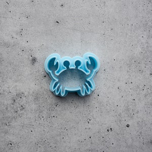 Puede incluir: Un cortador de galletas con forma de cangrejo de plástico azul claro.