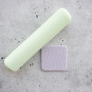 May include: A light green rolling pin with a wavy texture and a light purple square textured mat.