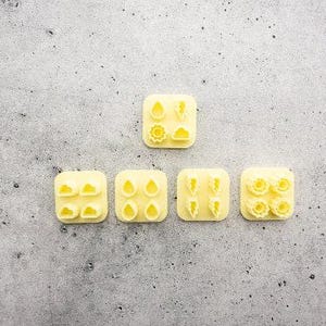 May include: A set of five pale yellow plastic cookie cutters. One square cutter features four distinct weather shapes: a raindrop, lightning bolt, sun, and cloud. Four additional square cutters each contain four identical shapes of clouds, raindrops, lightning bolts, or suns.