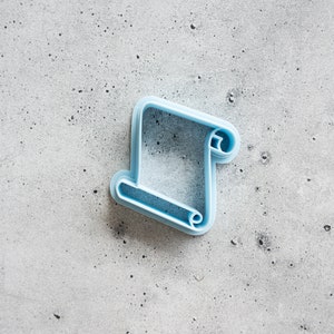 May include: A light blue plastic cookie cutter shaped like a scroll.
