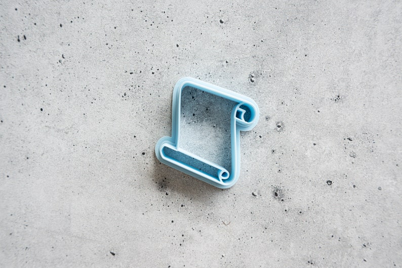 May include: A light blue plastic cookie cutter shaped like a scroll.