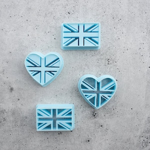 May include: Four blue plastic cookie cutters shaped like a heart and a square, each with a Union Jack design.