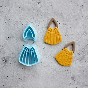 Puede incluir: Dos cortadores de galletas de pl&aacute;stico azul con forma de corona y falda, y dos decoraciones de fondant amarillo con forma de borlas.