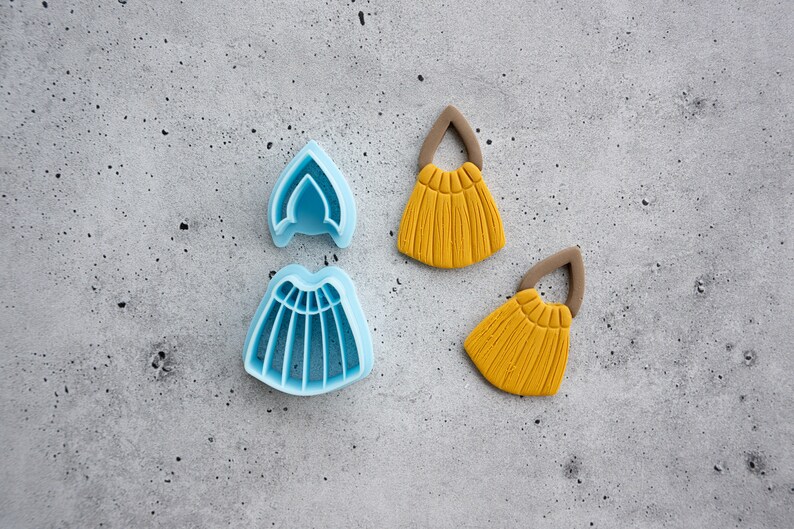 Puede incluir: Dos cortadores de galletas de pl&aacute;stico azul con forma de corona y falda, y dos decoraciones de fondant amarillo con forma de borlas.