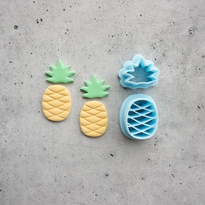 May include: Two yellow and green fondant pineapple decorations and three blue plastic pineapple cookie cutters on a gray background.