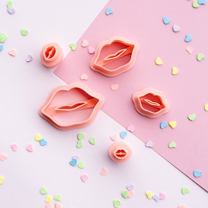 Peut inclure: Un ensemble de quatre emporte-pièces en plastique rose en forme de lèvres. Les emporte-pièces sont disposés sur un fond rose et blanc avec des confettis colorés.