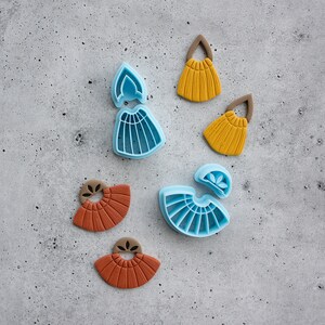 Puede incluir: Un juego de seis cortadores de pendientes de arcilla polim&eacute;rica. Dos cortadores son azules y presentan una forma de abanico con un peque&ntilde;o detalle de flor. Dos cortadores son marrones y presentan una forma de abanico con un peque&ntilde;o detalle de flor. Dos cortadores son amarillos y presentan una forma de abanico con un peque&ntilde;o detalle de flor.