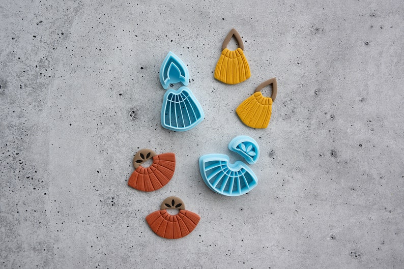 Puede incluir: Un juego de seis cortadores de pendientes de arcilla polim&eacute;rica. Dos cortadores son azules y presentan una forma de abanico con un peque&ntilde;o detalle de flor. Dos cortadores son marrones y presentan una forma de abanico con un peque&ntilde;o detalle de flor. Dos cortadores son amarillos y presentan una forma de abanico con un peque&ntilde;o detalle de flor.