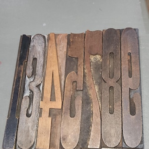 May include: A wooden printing block with the numbers 3, 4, 5, 6, 7, 8, and 9. The numbers are in a serif font and are made of various shades of brown wood. The block is rectangular and has a dark wooden frame.