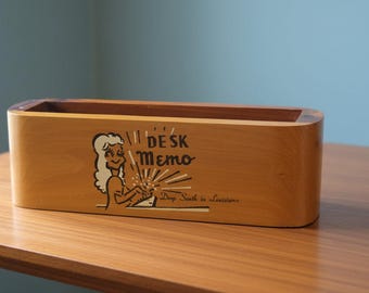 May include: A rectangular wooden desk memo holder with rounded edges. The front features a graphic illustration of a person typing at a desk, the text "DESK Memo" in a stylized font, and the smaller text "Deep South in Louisiana" below it.