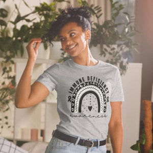 Może przedstawiać: Szary T-shirt z czarno-białym wzorem tęczy z napisem "Świadomość niedoboru odporności".