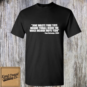 May include: Black t-shirt with white text that reads "JONE WASTE YORE TOYE MONME YORALL REDIII THE VOICE INSOIDE MOYE YEDD" - Tom DeLonge, 2004