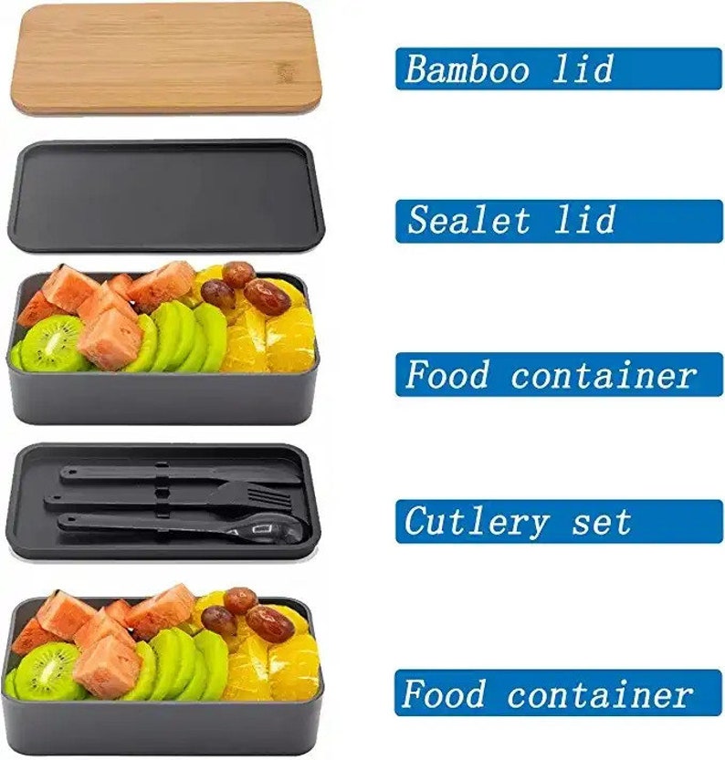 May include: A gray and black lunchbox set with two food containers, a cutlery set, a black sealable lid, and a bamboo lid. The lunchbox is filled with fruit, including watermelon, kiwi, and oranges.