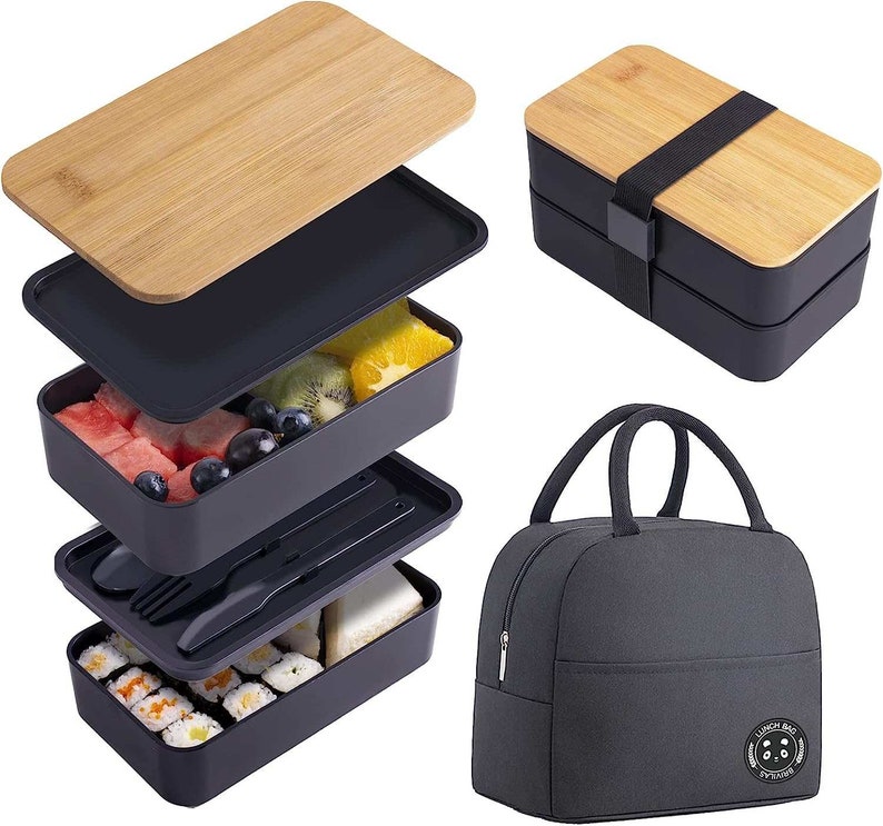 May include: A black and bamboo bento box with three tiers and a matching insulated lunch bag. The bento box has a removable lid and is filled with fruit, sushi, and other snacks. The lunch bag has a black fabric exterior with a white logo that says "Lunch Bag".