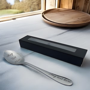 May include: A silver spoon with the text "Any Text Here" engraved on the front and back. The spoon is in a black box with a clear window.