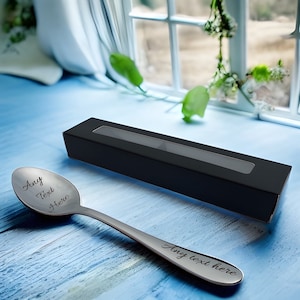 May include: A silver spoon with the text "Any Text Here" engraved on it. The spoon is in a black box with a clear window.