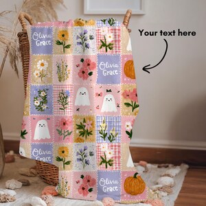 May include: A soft throw blanket featuring a patchwork grid design with pastel colors. The pattern includes illustrations of sunflowers, daisies, pink flowers, orange pumpkins, and white ghosts. The name Olivia Grace is printed in white script.