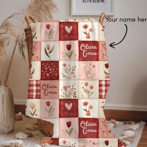 May include: A patchwork quilt with a floral design in red, pink, and cream. The quilt features squares with tulips, hearts, and floral arrangements. The name "Olivia Grace" is printed on the quilt.