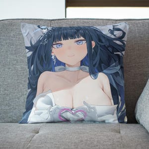 May include: A decorative pillow featuring an anime-style illustration of a woman with long black hair, wearing a white dress and holding a pink heart. The pillow is on a gray couch.