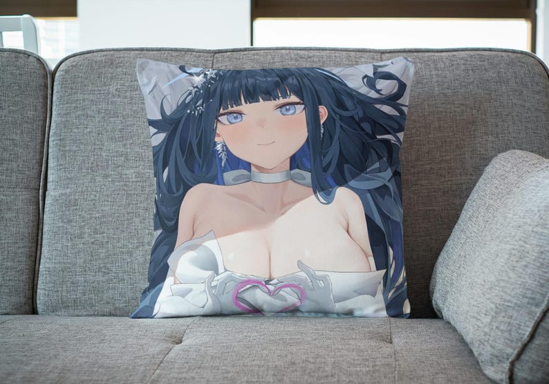 May include: A decorative pillow featuring an anime-style illustration of a woman with long black hair, wearing a white dress and holding a pink heart. The pillow is on a gray couch.