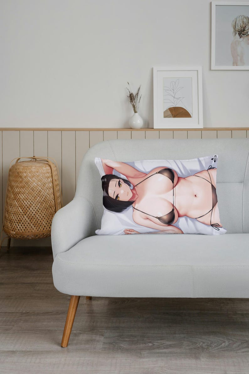 May include: A decorative pillow with a printed image of a woman wearing a black bikini. The pillow is on a light gray couch with wooden legs.