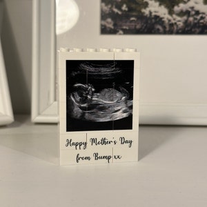 Könnte beinhalten: Weißer Lego-Stein mit einem Schwarzweiß-Ultraschallbild eines Babys. Der Text "Happy Mother's Day from Bump xx" ist auf der Unterseite des Steins aufgedruckt.