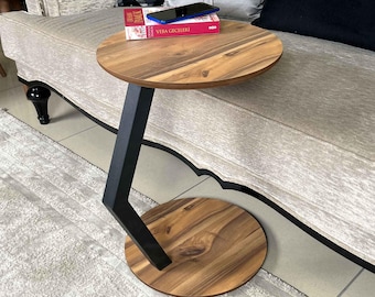 Puede incluir: Una mesa auxiliar redonda de madera con una base de metal negro. La mesa tiene un diseño único con una pata curva y una parte superior redonda. La mesa es perfecta para una sala de estar o un dormitorio.