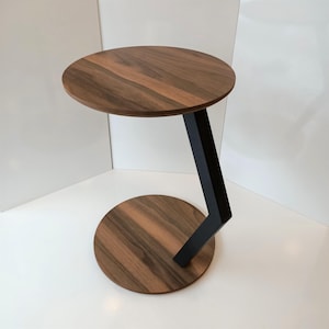 May include: A contemporary side table featuring a circular walnut top and base, linked by a black metal angled support. The table's design is minimalist, showcasing natural wood grain. The table's height is approximately 50 cm.