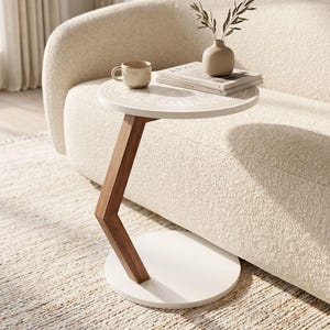 Può includere: Un tavolino a forma di C con un piano rotondo bianco caratterizzato da un motivo mandala inciso, una gamba di supporto angolare in legno scuro e una base circolare bianca. Il tavolo ospita una tazza in ceramica beige, un vaso e due libri.
