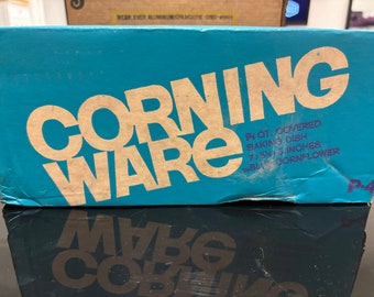 May include: A blue box with the text "CORNING WARE" in brown lettering. The box is labeled "1 1/2 Qt. Covered Baking Dish 7 x 5 1/2 x 1 3/4 inches The Blue Cornflower P-4"