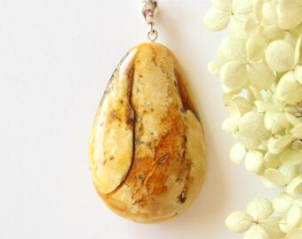 May include: A teardrop-shaped amber pendant with a silver bail. The amber is a light yellow color with brown and white inclusions.