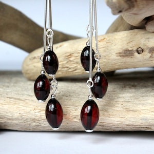 May include: A pair of silver dangle earrings with three dark red oval-shaped beads on each earring.